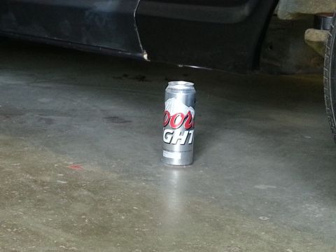 1967 Ford F-100 - A Coors Light can sits on a concrete floor near the undercarriage of a vehicle.