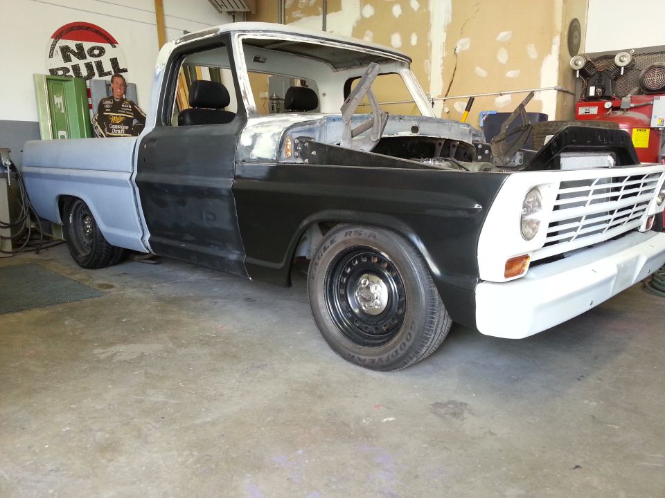 1967 Ford F-100 pickup truck undergoing restoration in a garage, primer and black paint on body panels