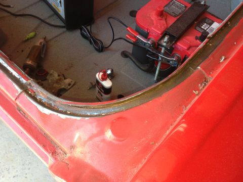 1964 Ford Fairlane - Car battery and charger are connected to a red car's door edge, showing signs of rust and wear.