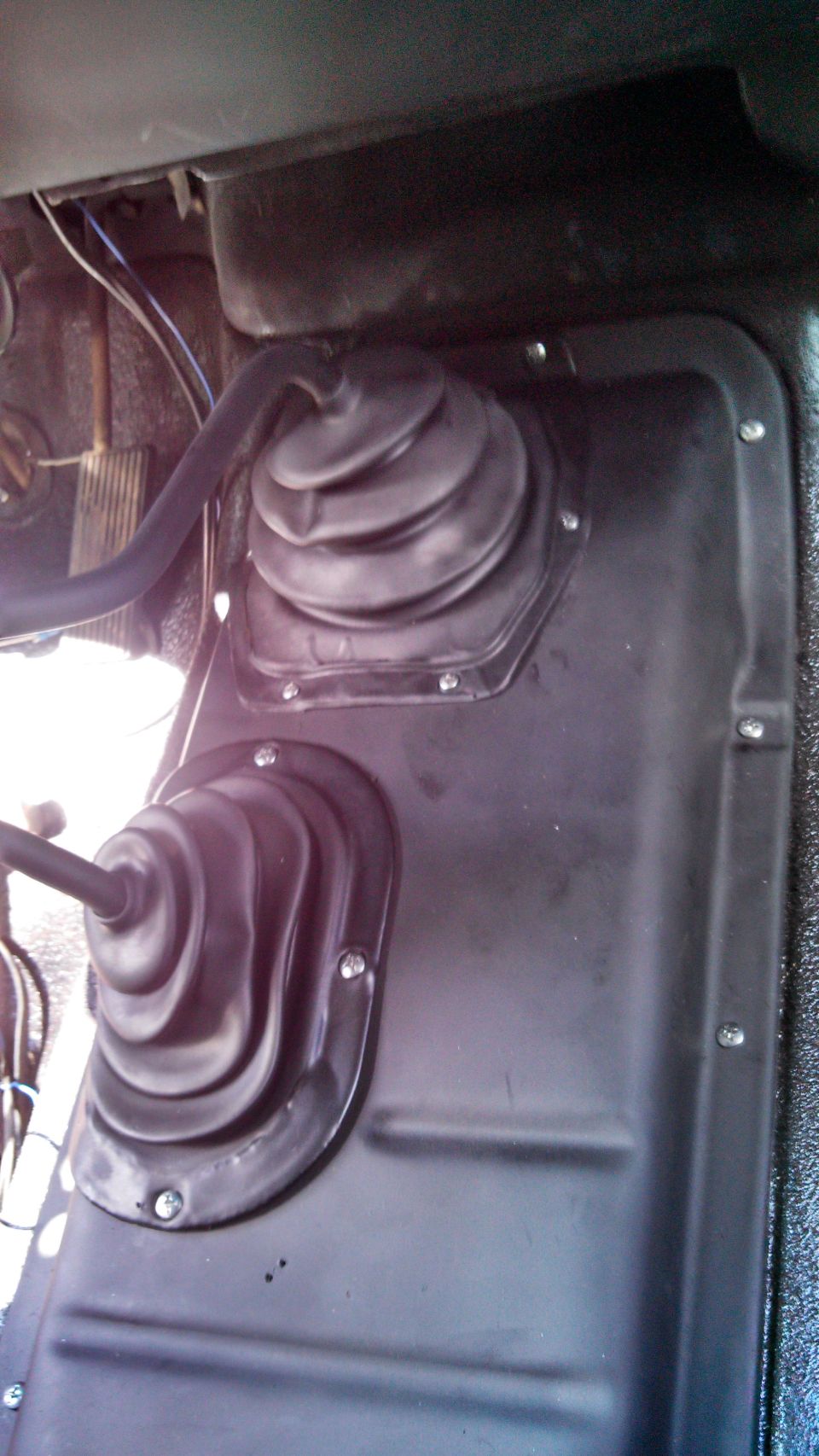 Interior shot of two rubber shifter boots on a vehicle floor. One is larger than the other