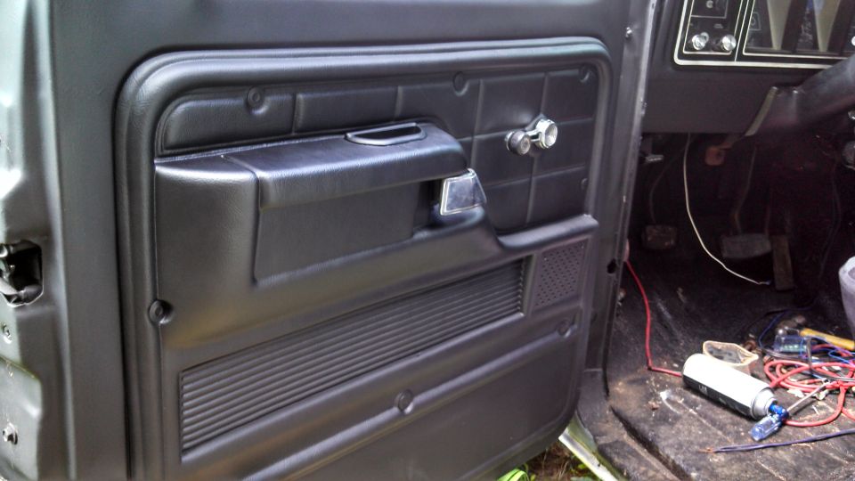 Black interior door panel with chrome handle and window crank, showing part of the dashboard and floor