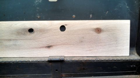 1979 Ford Bronco - A close-up view of a wooden plank with drilled holes, mounted inside a dark container.