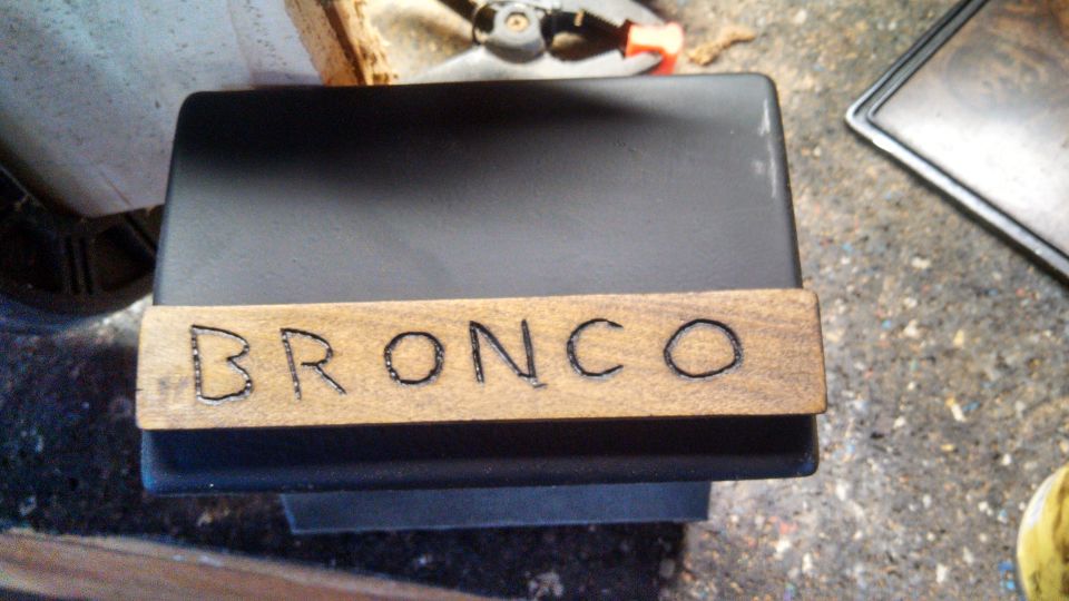 Wooden nameplate with 'BRONCO' burned into it, resting on a black object