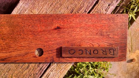 1979 Ford Bronco - A wooden plank with a carved piece of wood displaying the word Bronco is shown outdoors.