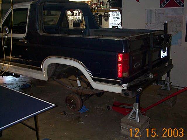 Dark Ford SUV on jack stands in garage with rear axle exposed for a swap