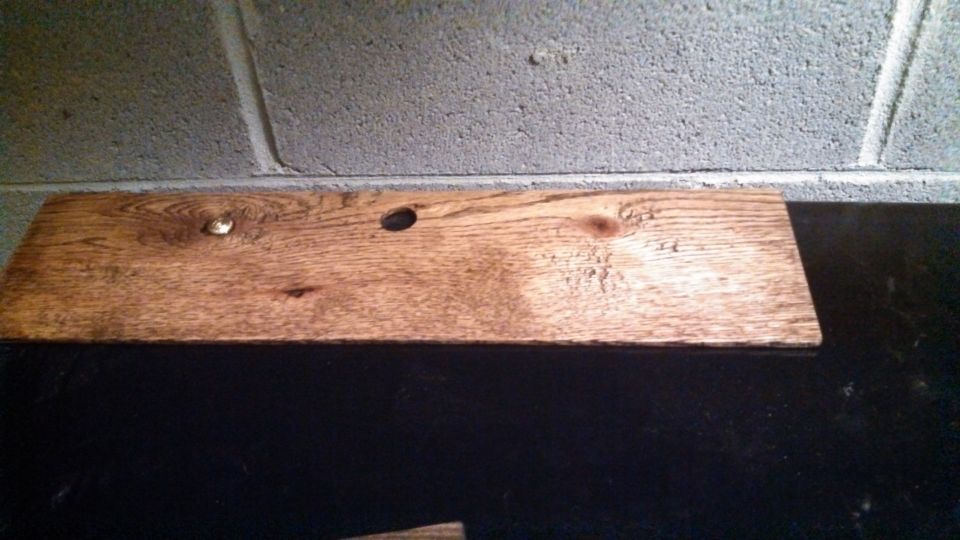 Wooden plank with a nail and two holes against a cinder block wall