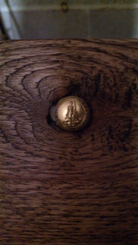 1979 Ford Bronco - Close-up of a gold emblem a figure, set against a dark wood grain background.