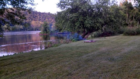 1979 Ford Bronco - A peaceful waterside scene with a campfire smoldering on the lawn.