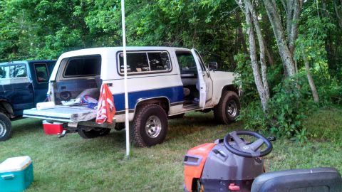 1979 Ford Bronco - A white and blue SUV with its tailgate down is parked next to another vehicle in a wooded area.