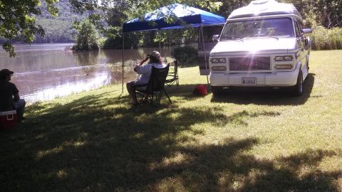 1979 Ford Bronco - A GMC van is parked near a lake where two people are relaxing under a canopy.