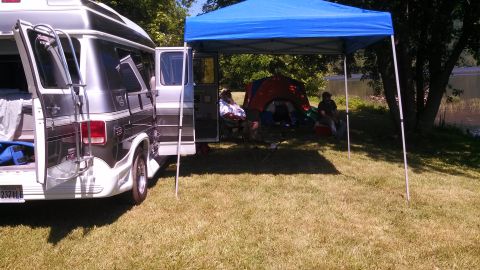 1979 Ford Bronco - People are relaxing at a campsite next to a camper van under a blue canopy.
