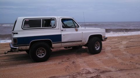 1979 Ford Bronco - This SUV, likely from the 1970s or 1980s, sits on a beach with waves in the background.