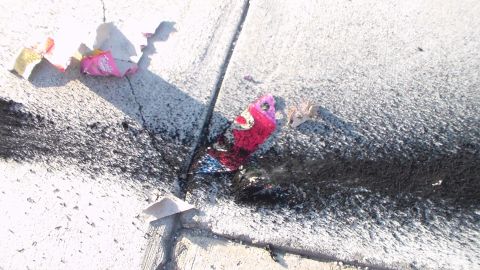 2003 Ford Crown Victoria - Spent firework wrappers and scorch marks litter a cracked concrete surface in bright sunlight.