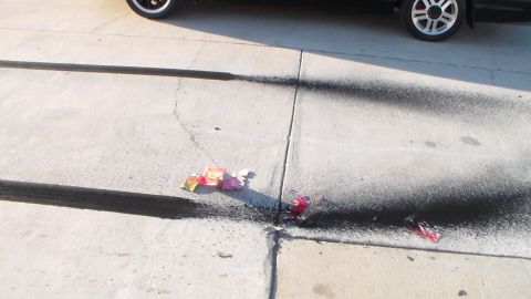 2003 Ford Crown Victoria - Charred firework remnants and burn marks scatter across a concrete lot beside the wheel of a parked car.