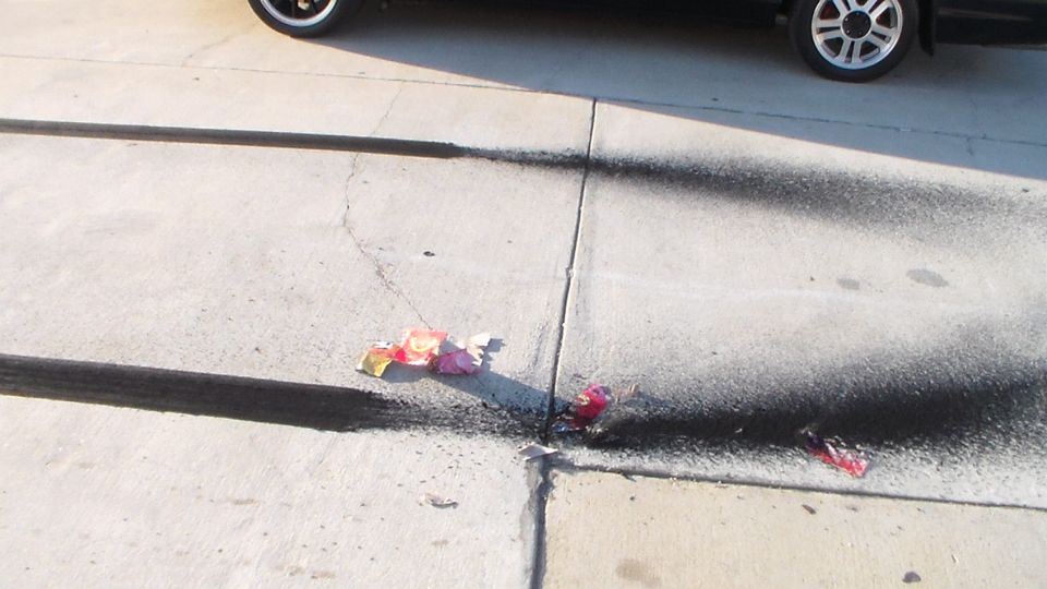 Burnt firework debris and scorch marks on concrete near a parked car