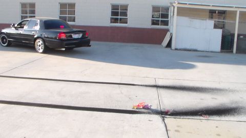 2003 Ford Crown Victoria - black sedan parks in a concrete lot near a building, with spent firework debris and scorch marks on the pavement.