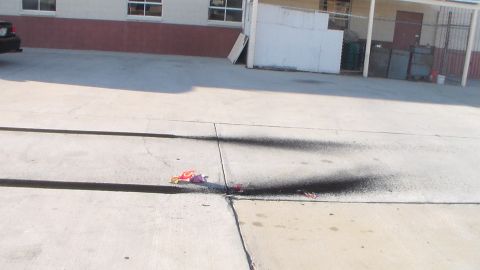 2003 Ford Crown Victoria - Spent firework wrappers and a dark scorch streak mark a concrete lot beside an industrial building.