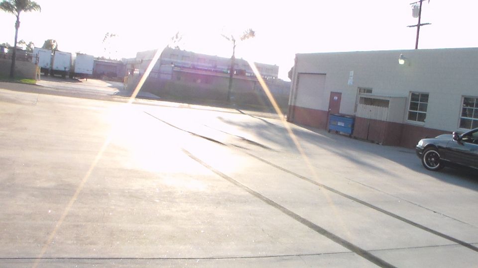 Sunlit industrial lot with parked dark car and lens flare