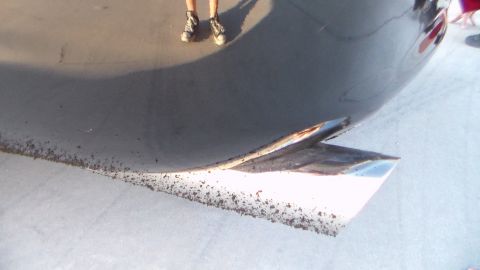 2003 Ford Crown Victoria - close-up of a dark car's dirt-speckled rocker panel, with a person's sneakered feet visible in the background.