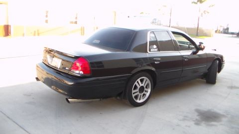 2003 Ford Crown Victoria - black full-size sedan photographed from the rear three-quarter angle on a paved lot, with sticker decals on the rear window.