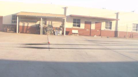 2003 Ford Crown Victoria - bright, washed-out shot of a concrete industrial yard with a covered storage bay and tan warehouse buildings.