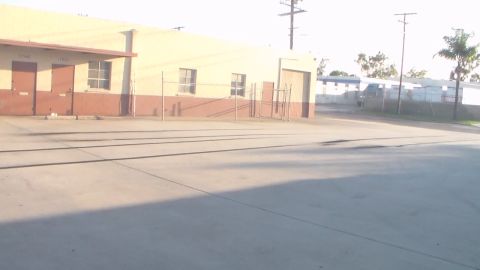 2003 Ford Crown Victoria - bright, hazy view of an empty paved lot in front of a tan warehouse building with chain-link fencing.