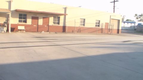 2003 Ford Crown Victoria - washed-out, sunlit shot of an empty concrete yard fronting a long tan warehouse with brick-trimmed bays.