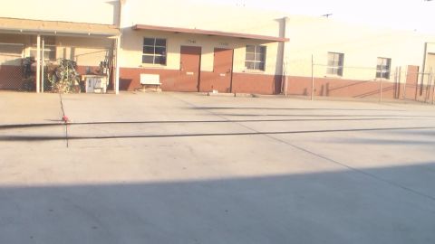 2003 Ford Crown Victoria - hazy, overexposed view of an empty paved industrial yard in front of a tan warehouse and chain-link fencing.