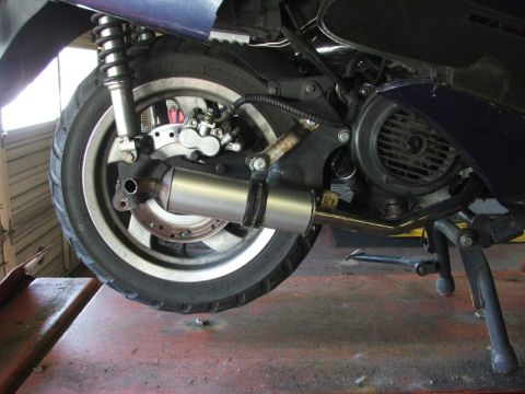 2008 Yamaha Zuma - Close-up view of a scooter's exhaust system and rear wheel, showing the muffler and brake components.