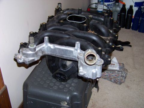 1999 Mercury Grand Marquis - An intake manifold is shown resting on a black container, with various bottles and cans visible in the background.