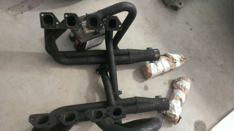Two sets of black exhaust headers and mufflers on a concrete floor