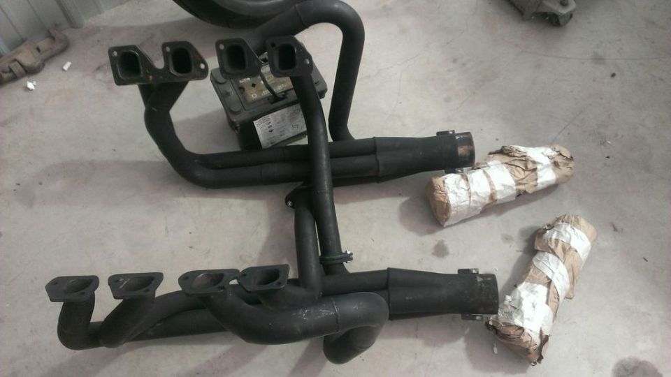 two sets of black exhaust headers and mufflers on a concrete floor, some wrapped in paper