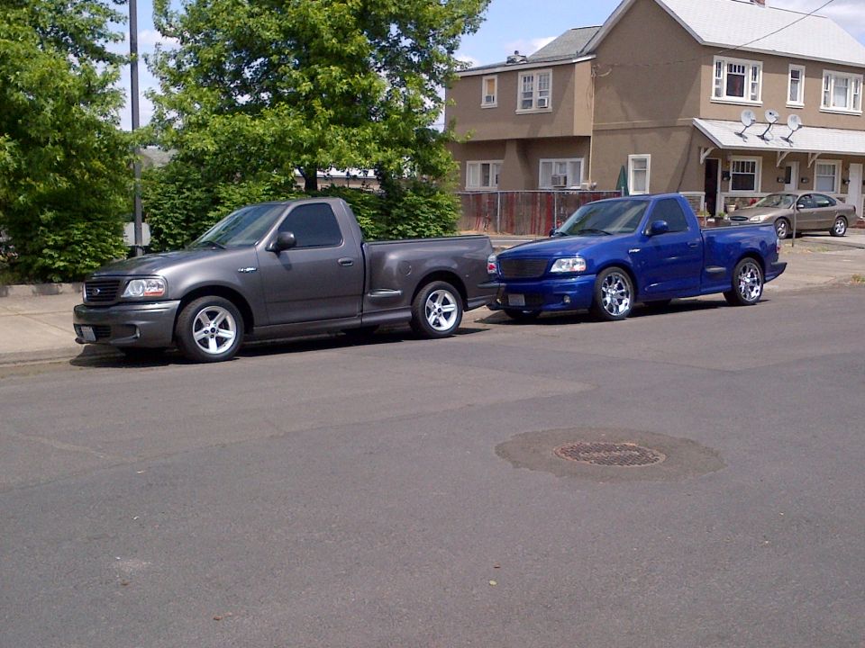 Two Ford F-150 Lightning trucks parked on a street, one gray and one blue