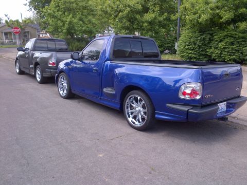 2003 Ford F-150 - A blue 2003 Ford F-150 Lightning pickup truck is parked behind a gray pickup truck on a residential street.