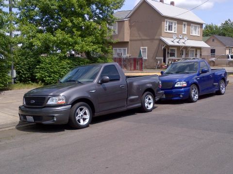 2003 Ford F-150 - A pair of Ford F-150 Lightning pickup trucks, one gray and one blue, are parked side-by-side on a residential street.