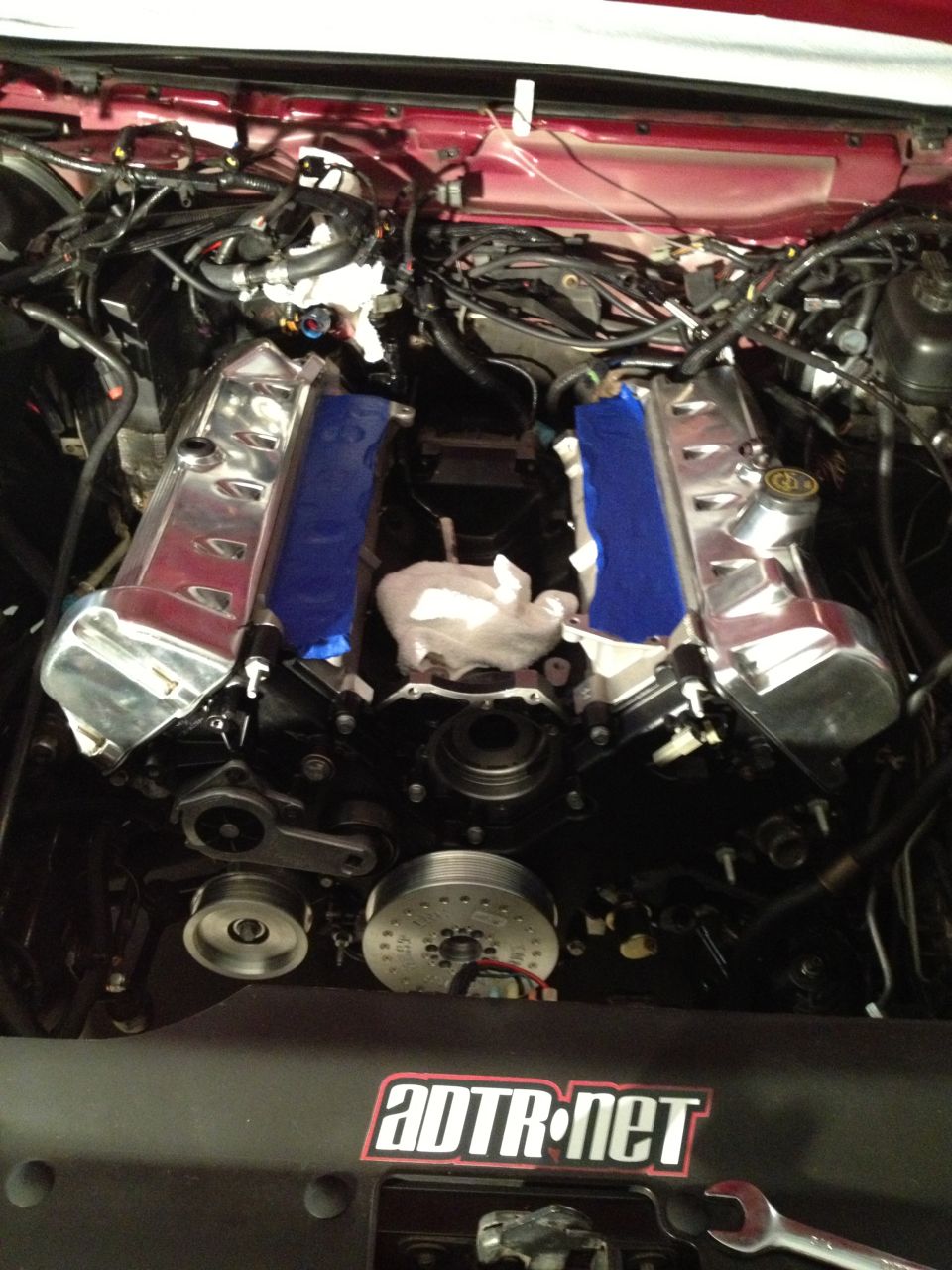 Engine bay with chrome valve covers and blue tape, ADTR.net sticker visible