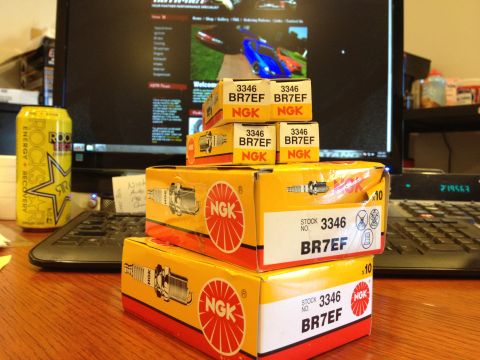 1992 Ford Crown Victoria - Several boxes of NGK BR7EF spark plugs are stacked on a wooden desk.
