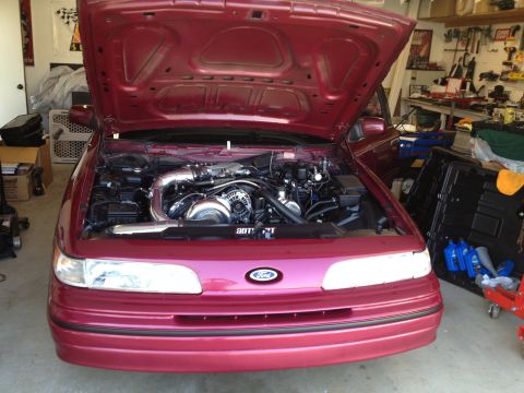 1992 Ford Crown Victoria - The engine bay of a red Ford Crown Victoria, a prominent turbocharger and custom piping.