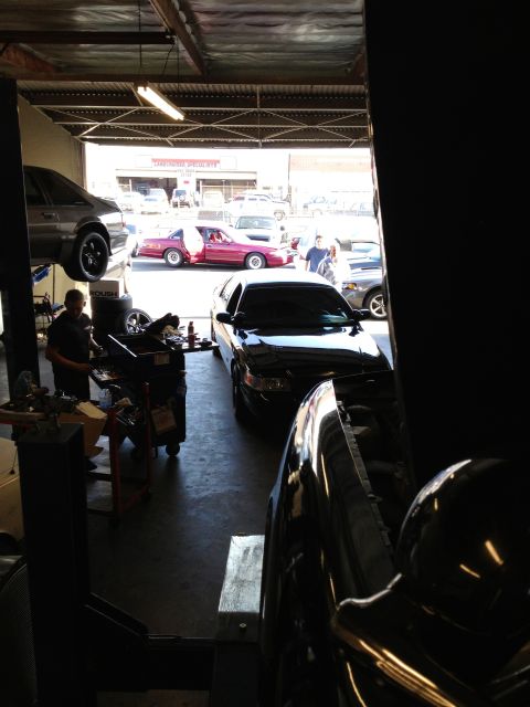 1992 Ford Crown Victoria - A mechanic works in a garage bay with several vehicles present, including a black sedan on a lift.