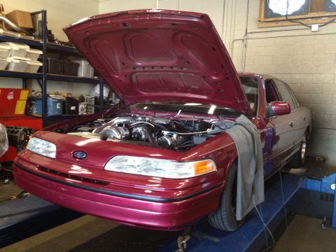 1992 Ford Crown Victoria - A maroon 1992 Ford Crown Victoria is positioned on a dynamometer with its hood open, a heavily modified engine.