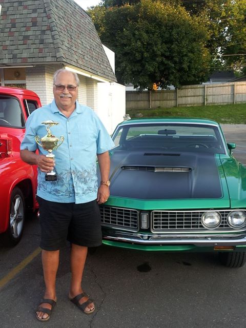 1971 Ford Ranchero - A man holds a trophy next to a green coupe with a black hood scoop, possibly a 1970s model.