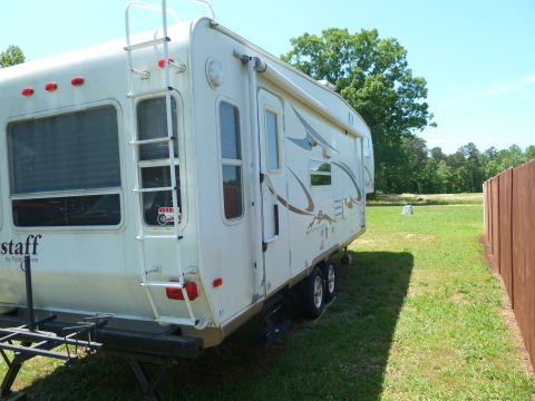 1992 Ford Mustang - Fifth wheel camper parked outdoors on a sunny day, with a wooden fence to the right.