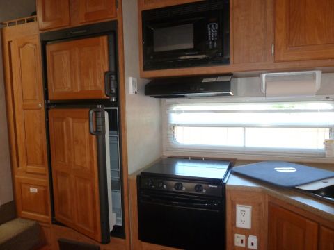 1992 Ford Mustang - Interior view of a camper kitchen wooden cabinetry, a black stove, and a refrigerator.