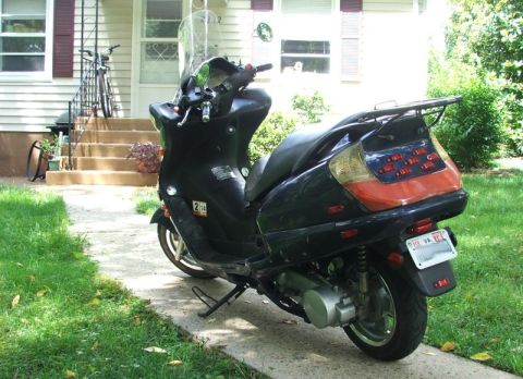 2008 Yamaha Zuma - A black scooter is parked on a concrete path next to a lawn, with a house in the background.