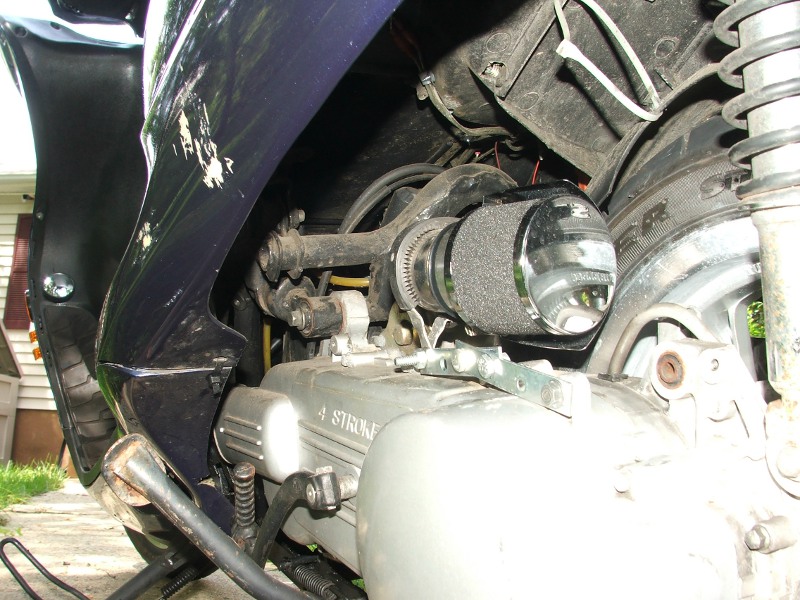 Scooter engine bay with a chrome-capped aftermarket air filter attached to the intake