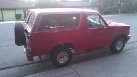 1988 Ford Bronco - This red SUV, likely a 1992 model, is viewed from the side with a spare tire mounted on the rear.