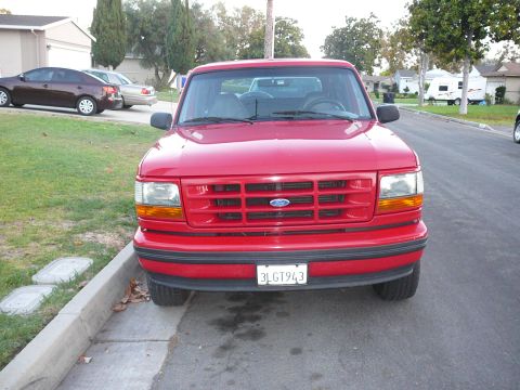 1988 Ford Bronco - This red Ford truck is parked on a residential street. The grille and headlights indicate it is from the mid-1990s.