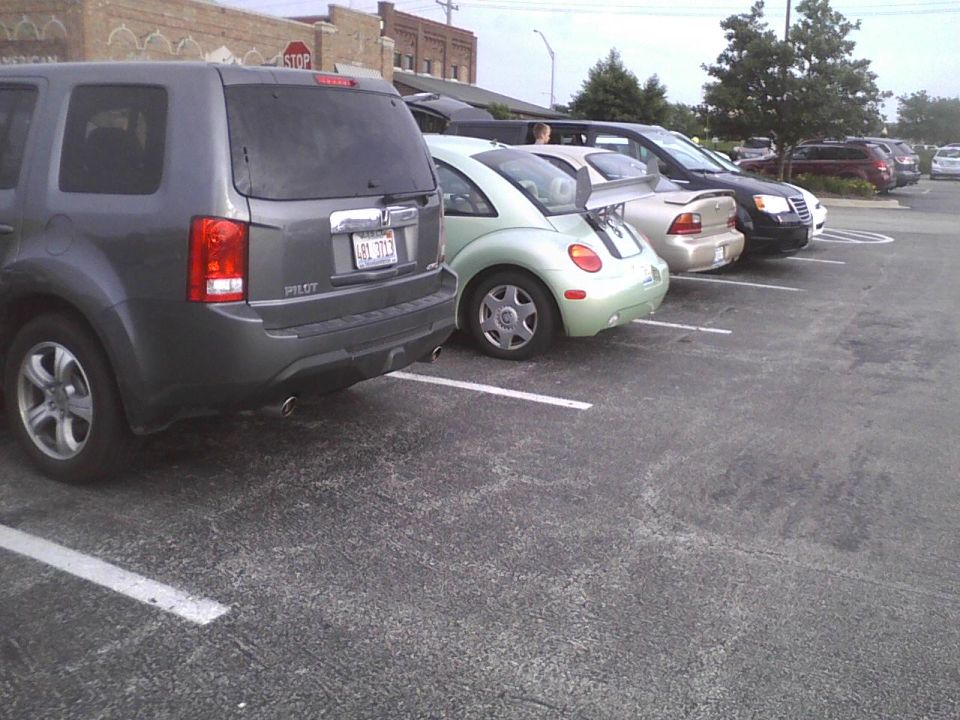 Parked cars including a gray SUV, a light green Volkswagen Beetle with a spoiler, and a silver sedan
