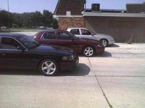 2003 Ford Crown Victoria - Three Ford Crown Victorias are parked in a row on a sunny day.