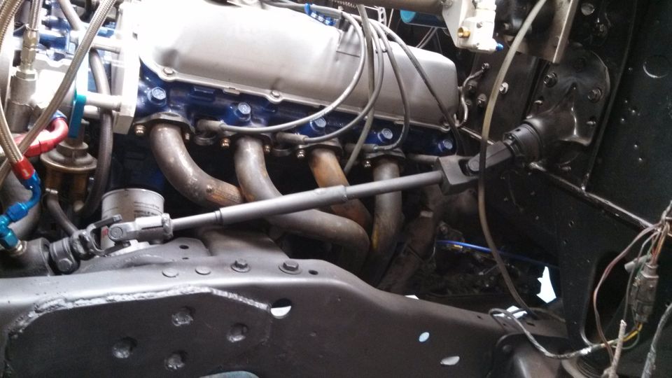 Close-up of a V8 engine with custom headers and fuel lines. Steering linkage visible